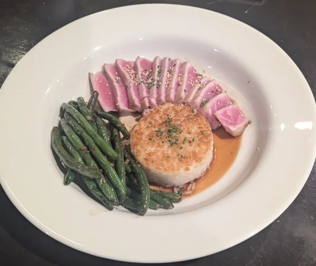 Seared tuna steak served with green beans and a rice cake.