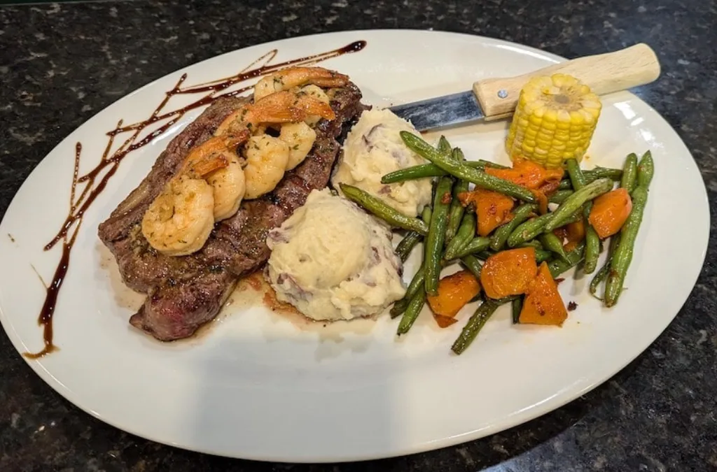 Surf and turf featuring Ribeye steak and grilled shrimp with corn.